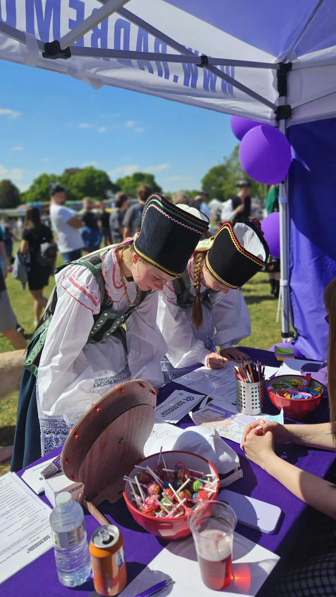 Two young girls in traditional Polish outfits coloring RAD Removals graphics at the RAD stall during Polish Heritage Day 2025 in Hounslow, promoting movers West London and storage Ealing.